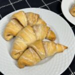 A plate of golden brown cinnamon sugar crescent rolls, filled with a buttery cinnamon and sugar filling and with a drizzle of vanilla glaze on top.